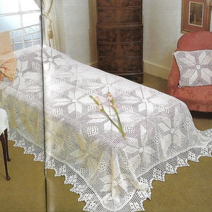 May include: A white crocheted bedspread with a delicate floral pattern. The bedspread has a scalloped edge and is laid out on a bed with a white sheet and a pillow.