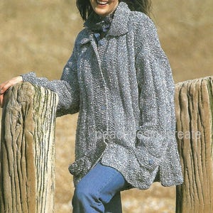 May include: A gray knitted cardigan with a button closure and a collar. The cardigan is worn by a person standing in front of a wooden fence.