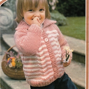 Peut inclure: Un cardigan tricoté rayé rose et blanc avec une fermeture boutonnée. Le cardigan a un col et est porté par un jeune enfant.