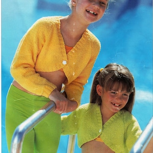 Peut inclure: Deux filles portant des cardigans courts en tricot jaune et vert. Les filles sourient et se tiennent près d'une piscine.