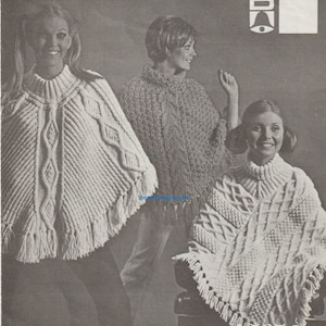 Könnte beinhalten: Drei Frauen präsentieren weiße Strickponchos mit Fransen. Die Ponchos haben ein Zopfmuster.