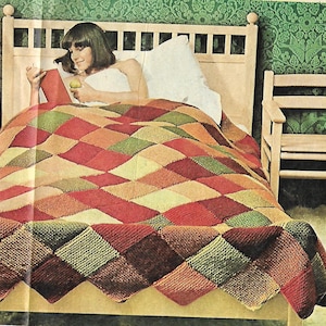 Könnte beinhalten: Eine mehrfarbige gestrickte Decke mit einem Rautenmuster in Rot-, Grün-, Braun- und Beigetönen. Die Decke liegt auf einem Bett mit einem weißen Kissen und eine Frau liegt im Bett und liest ein Buch.