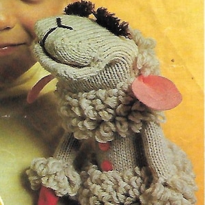 May include: A grey knitted puppet of a sheep with pink ears and red accents. The puppet is being held by a child.