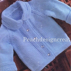 May include: A pale blue knitted baby cardigan with a rounded collar and button fastening. The sweater has a textured knit design and ribbed cuffs. The text "Peachdesigncreate" is visible on the garment.