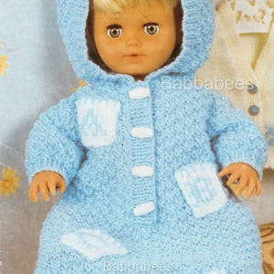 Könnte beinhalten: Eine Puppe in einem hellblauen Strickmantel mit Kapuze und weißen Akzenten. Der Mantel hat weiße quadratische Taschen und weiße Knöpfe. Der Text "Babbabees" ist sichtbar.