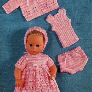 May include: A pink knitted doll outfit with a striped cardigan, dress, hat, nappy, and booties.