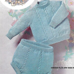 May include: A knitted baby sweater and pants set in a light blue color with a cable knit pattern. The set is laid out on a floral background. The text "CORRECT PLYS AND SIZES INSIDE" is visible at the bottom of the image.