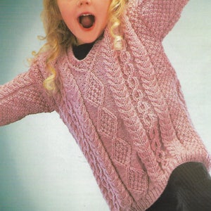 Könnte beinhalten: Ein rosa gestrickter Pullover mit einem Zopfmuster. Der Pullover hat einen V-Ausschnitt und lange Ärmel.