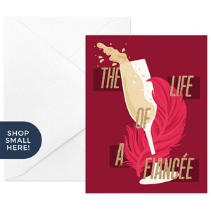May include: A burgundy greeting card with a champagne glass design and the text "THE LIFE OF A FIANC&Eacute;E" in gold. A white envelope is on the left. The image includes a pink feather and bubbly liquid.