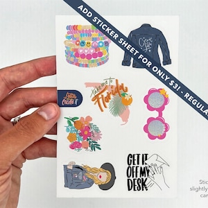 May include: A sticker sheet featuring various colorful designs, including a denim jacket, floral arrangements, sunglasses, and the phrase "Take me to Florida." The sheet is held by a hand.