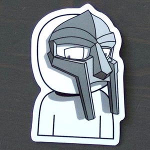 May include: A sticker featuring a stylized illustration of a figure wearing a gray mask and hood. The mask has a distinctive angular design with long, rectangular features. The figure is depicted in shades of gray and white, with a black outline.
