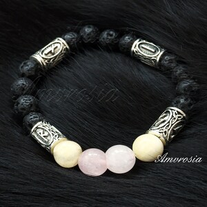 Op de afbeelding: Een armband van zwarte lavasteen met zilveren kralen en twee roze rozenkwarts kralen. De zilveren kralen hebben Keltische knoopontwerpen en runen.