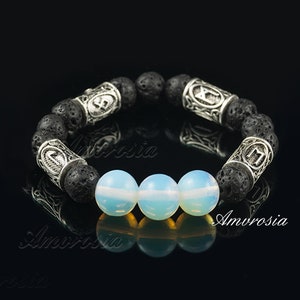 Puede incluir: Un brazalete de roca de lava negra con cuentas de plata que presentan un símbolo en cada cuenta. Tres cuentas de ópalo blanco están en el centro del brazalete.
