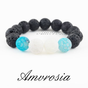 May include: A black lava rock bracelet with white and blue agate beads. The bracelet has the word "Amvrosia" written on it.