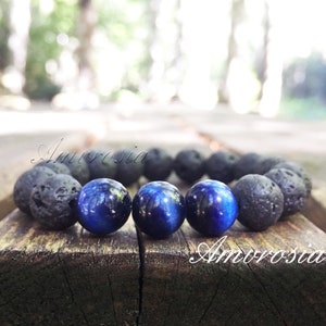 Pode incluir: Um bracelete feito com contas de rocha de lava preta e contas de olho de tigre azul. O bracelete está sobre uma superfície de madeira.