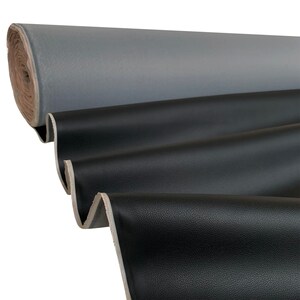 Peut inclure: Un rouleau de tissu gris est visible en arri&egrave;re-plan, avec un tissu noir au premier plan. Le tissu noir est drap&eacute; en plis souples, r&eacute;v&eacute;lant une surface textur&eacute;e. Les bords du tissu sont visibles.