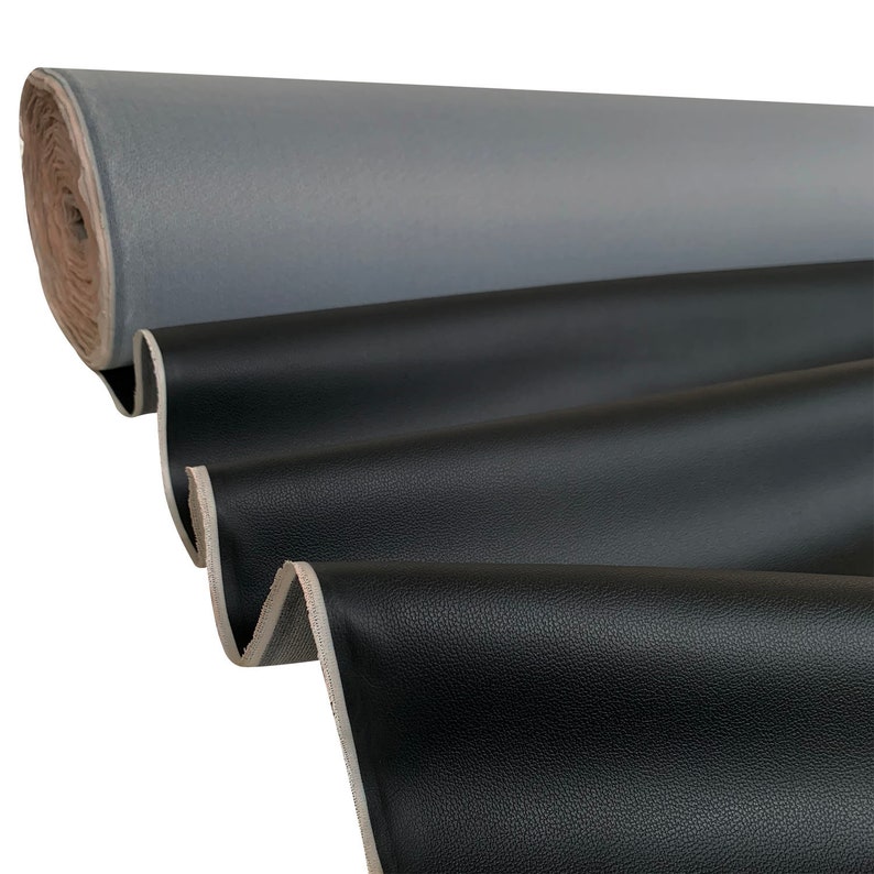 Peut inclure: Un rouleau de tissu gris est visible en arri&egrave;re-plan, avec un tissu noir au premier plan. Le tissu noir est drap&eacute; en plis souples, r&eacute;v&eacute;lant une surface textur&eacute;e. Les bords du tissu sont visibles.