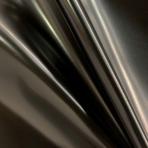 May include: Black fabric with a smooth, shiny finish. The fabric is folded and draped, creating soft curves and folds.