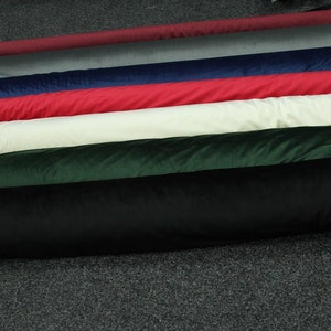 May include: A collection of fabric rolls in various colors, including black, green, white, red, blue, gray, and burgundy. The fabric rolls are arranged in a stack, with the black roll at the bottom and the burgundy roll at the top.