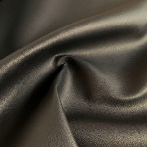 Peut inclure: Gros plan sur un tissu en cuir noir avec une surface textur&eacute;e. Le mat&eacute;riau est pli&eacute;, cr&eacute;ant des ombres et soulignant la texture souple. La couleur sombre et le lustre subtil sugg&egrave;rent un mat&eacute;riau de haute qualit&eacute;.