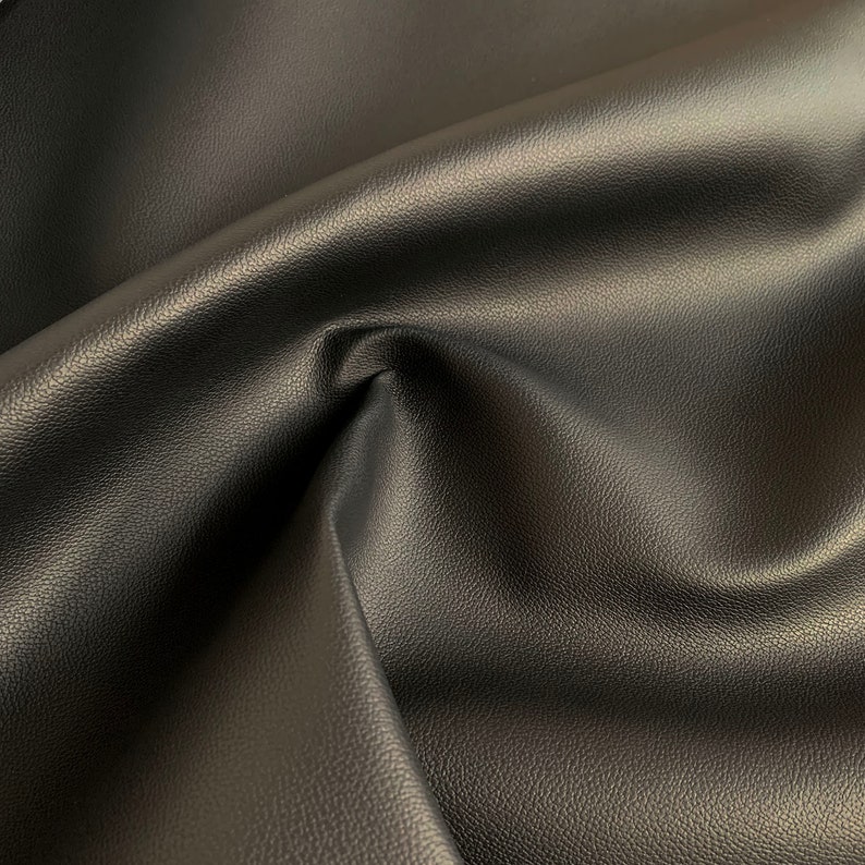 Peut inclure: Gros plan sur un tissu en cuir noir avec une surface textur&eacute;e. Le mat&eacute;riau est pli&eacute;, cr&eacute;ant des ombres et soulignant la texture souple. La couleur sombre et le lustre subtil sugg&egrave;rent un mat&eacute;riau de haute qualit&eacute;.