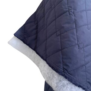 May include: Close-up of a dark blue quilted fabric with a white backing. The fabric has a diamond pattern and a frayed edge.
