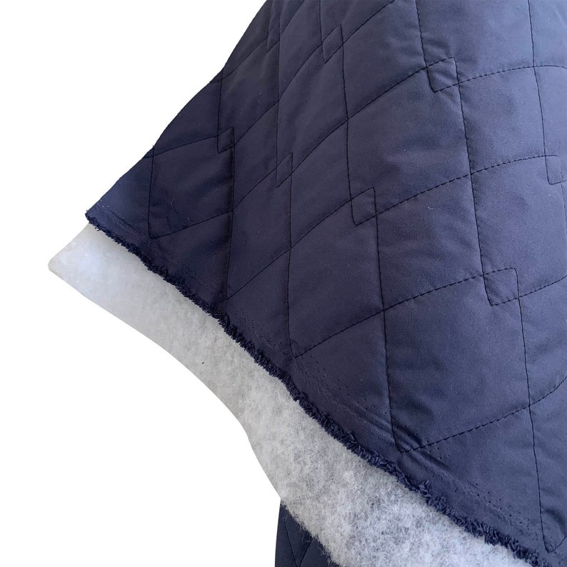 May include: Close-up of a dark blue quilted fabric with a white backing. The fabric has a diamond pattern and a frayed edge.