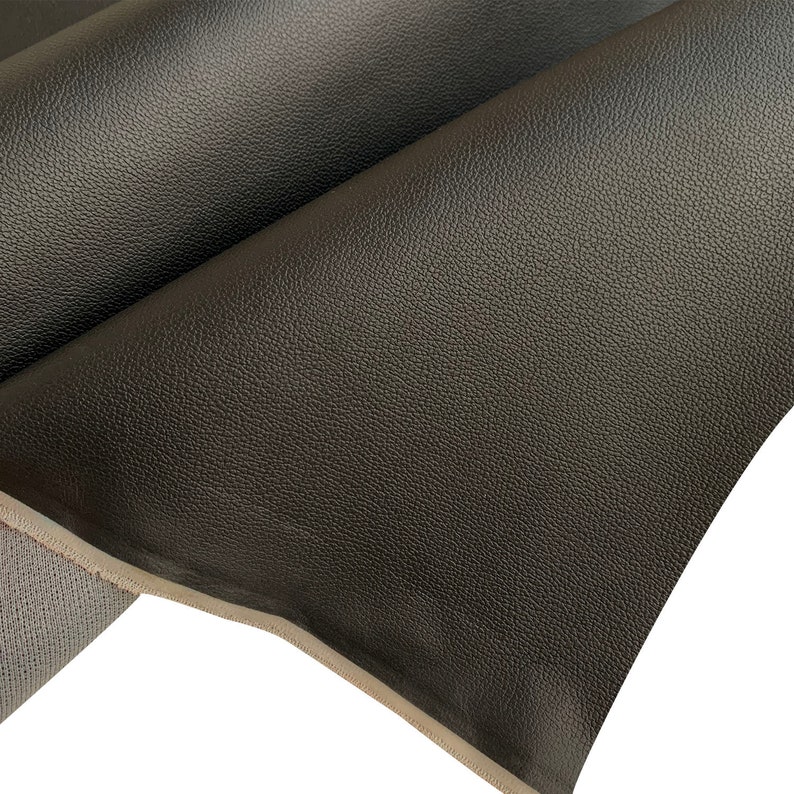 Peut inclure: Gros plan sur deux feuilles de cuir gris fonc&eacute; qui se chevauchent. Le cuir a une surface textur&eacute;e et granuleuse. Les bords du cuir sont visibles, r&eacute;v&eacute;lant un dos de couleur plus claire.
