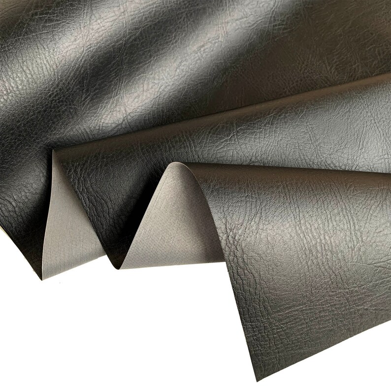 May include: Black faux leather fabric with a textured surface. The fabric is folded to show the back side, which is a smooth, gray material.