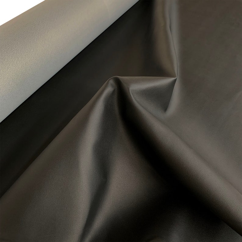 Peut inclure: Gros plan sur un tissu en cuir noir pli&eacute; avec une texture subtile. Le tissu est drap&eacute;, r&eacute;v&eacute;lant un dessous gris clair et une finition lisse et mate. L'&eacute;clairage met en valeur les plis et les ombres.