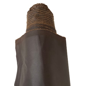 May include: A roll of dark brown fabric with a frayed edge. The fabric is rolled up tightly and the end of the roll is visible.