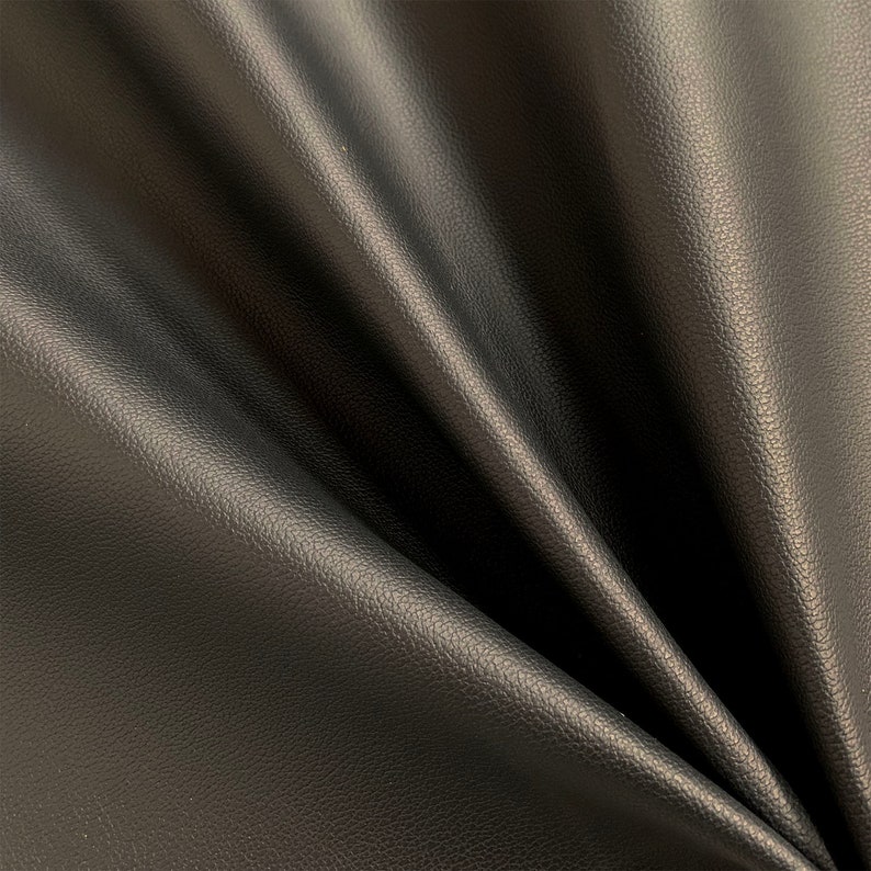 Peut inclure: Gros plan sur un tissu en cuir noir avec une surface textur&eacute;e. Le mat&eacute;riau est drap&eacute;, montrant des plis et des ombres qui mettent en valeur la texture souple. La couleur fonc&eacute;e sugg&egrave;re un mat&eacute;riau polyvalent.