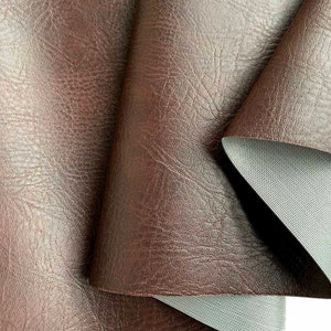 May include: Close-up of brown faux leather fabric with a textured surface. The fabric is folded over to show the gray backing.