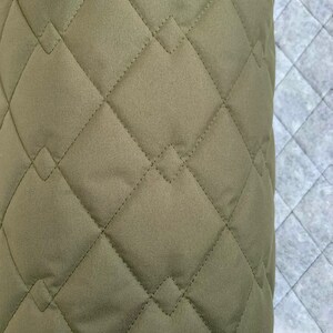 May include: Close-up of a green quilted fabric with diamond-shaped stitching. The fabric has a soft, textured surface.