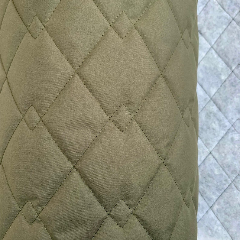 May include: Close-up of a green quilted fabric with diamond-shaped stitching. The fabric has a soft, textured surface.