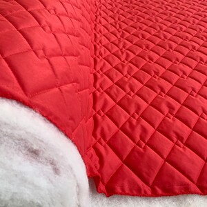 May include: Red quilted fabric with a diamond pattern. The fabric is folded over and the underside is white.