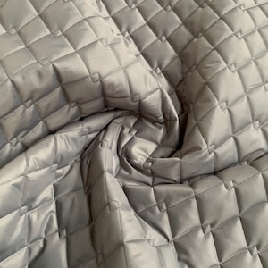 May include: A close-up of a gray quilted fabric with a diamond pattern. The fabric is soft and has a subtle sheen.