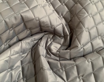 May include: A close-up of a gray quilted fabric with a diamond pattern. The fabric is soft and has a subtle sheen.