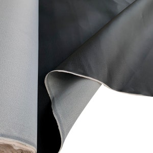 Peut inclure: Un rouleau de tissu gris et un morceau de mat&eacute;riau noir semblable &agrave; du cuir. Le mat&eacute;riau noir est pli&eacute;, r&eacute;v&eacute;lant un dessous gris. Les textures des deux mat&eacute;riaux sont visibles, le mat&eacute;riau simili cuir ayant une surface l&eacute;g&egrave;rement textur&eacute;e.