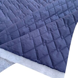 May include: A close-up of a dark blue quilted fabric with a diamond pattern. The fabric is folded over itself, revealing a white backing.