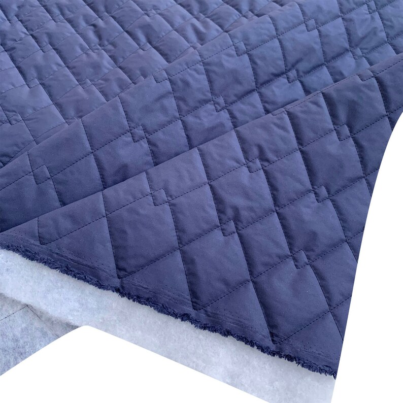 May include: A close-up of a dark blue quilted fabric with a diamond pattern. The fabric is folded over itself, revealing a white backing.