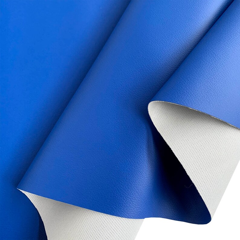 May include: A close-up of a blue faux leather fabric with a white backing. The fabric has a textured surface and is folded in half.