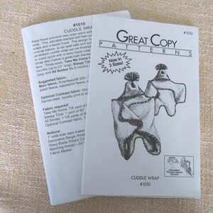 May include: Two white paper pattern sheets. The front sheet reads "Great Copy Patterns" and "Cuddle Wrap #1010" with a drawing of a baby wrap. The other sheet has text about the pattern, including fabric requirements.