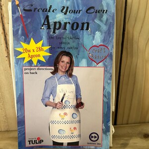 May include: A Create Your Own Apron craft kit package featuring a 50.8w x 71.1h cm apron. The blue packaging displays a finished white apron with a chicken and egg pattern, the text Which came first, and the Tulip brand logo by Innovo Inc.