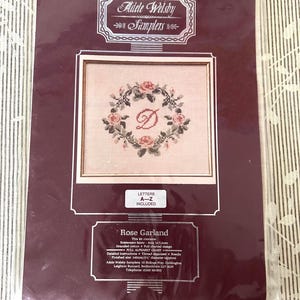 Peut inclure: Kit de point de croix "Rose Garland" d'Adele Welsby Samplers. Il présente un motif encadré de couronne florale avec la lettre "D". Le kit comprend les lettres A-Z et des instructions détaillées. Dimensions finies : 140 mm.