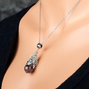 May include: A silver chain necklace with a pendant featuring a purple gemstone encased in a filigree design.