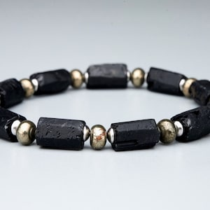 May include: Black Tourmaline and Pyrite beaded bracelet. The bracelet features black Tourmaline beads and gold Pyrite beads.