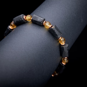 May include: A black and gold beaded bracelet with black rectangular beads and round gold beads.