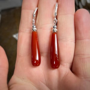 May include: A pair of dangle earrings with teardrop-shaped carnelian stones and silver hooks.