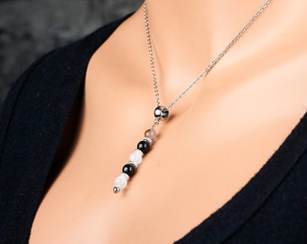 May include: A silver chain necklace with a pendant made of black, white, and pink beads. The pendant is attached to the chain with a silver bead.